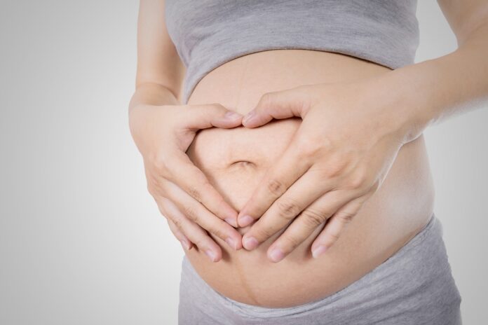 Pregnant Woman holding her hands in a heart shape on her baby bump.